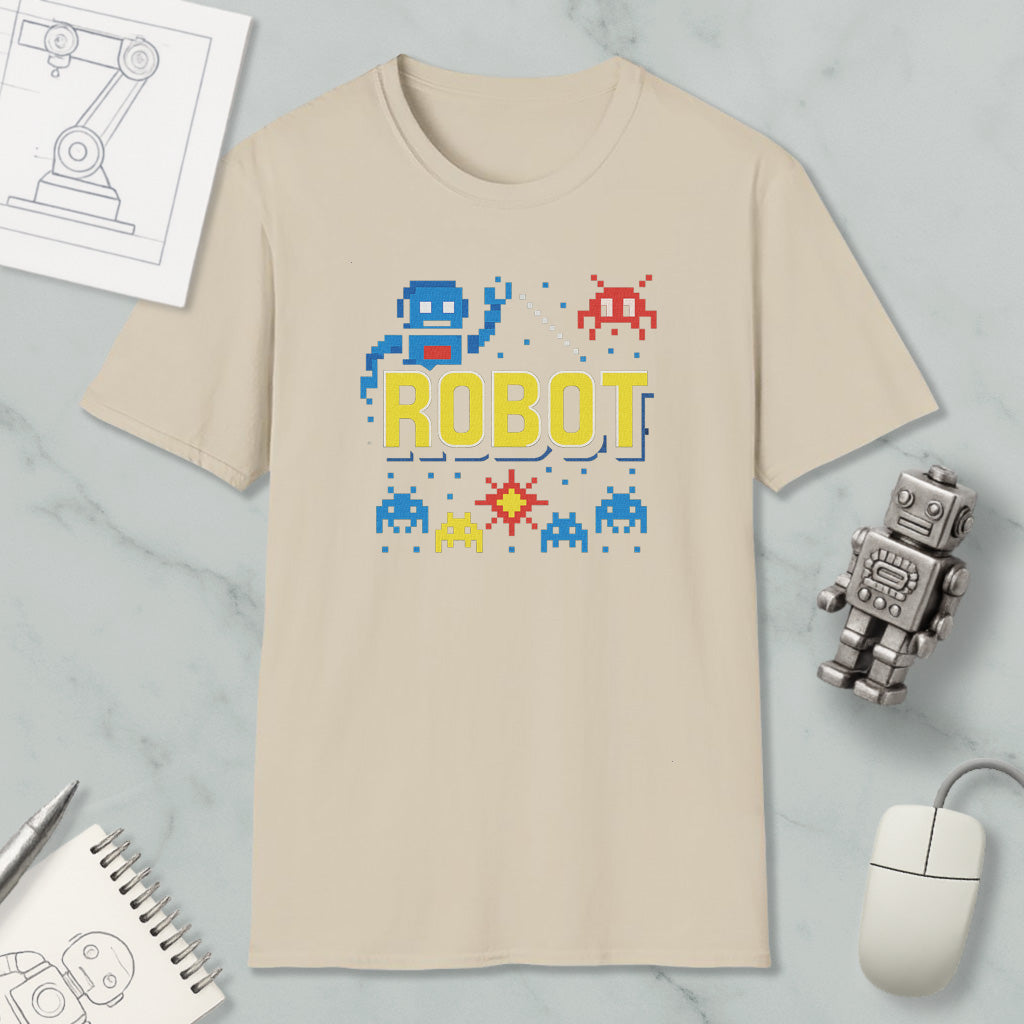 a beige t-shirt with a robot graphic and pixel art, along with a computer mouse, a notebook, and a small robot figurine.