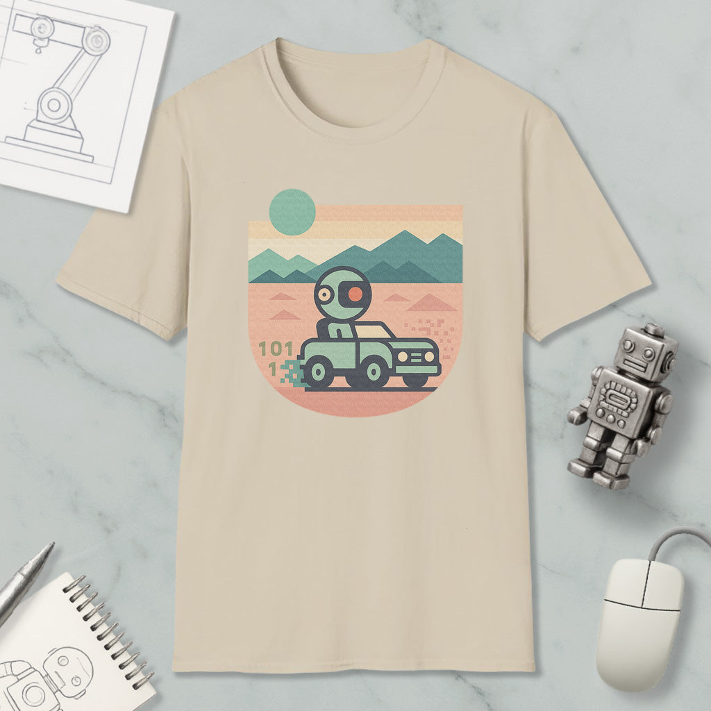 a beige t-shirt with a graphic design depicting a robot driving a car on a desert road, with mountains in the background. The t-shirt is surrounded by various objects, including a computer mouse, a notebook, and a small robot figurine.
