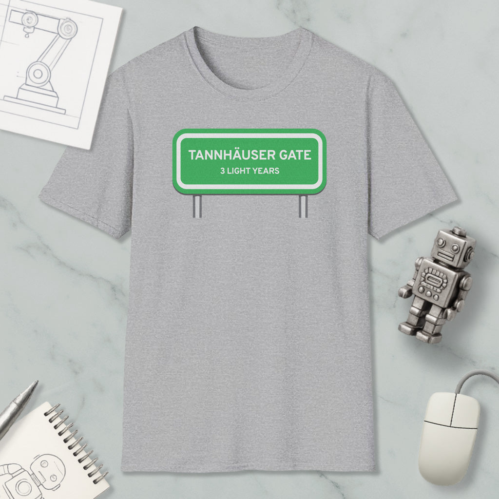 a gray t-shirt with a green highway sign that reads "Tannhäuser Gate 3 Light Years" printed on it. The t-shirt is placed on a marble surface, surrounded by various objects such as a computer mouse, a notebook, and a small robot.