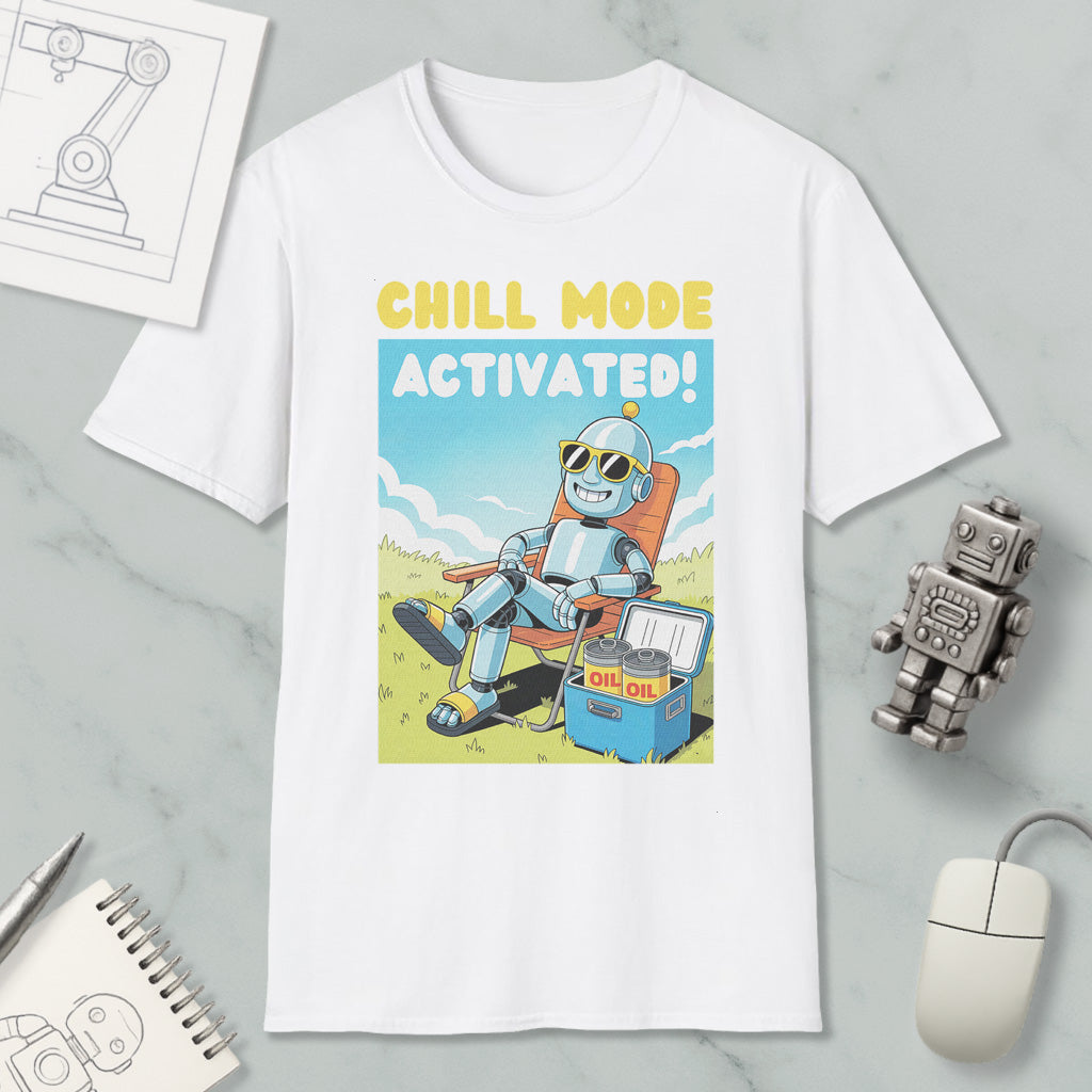 A white t-shirt with a cartoon robot sitting in a chair and holding a cooler, with the text "CHILL MODE ACTIVATED!" printed on it. The t-shirt is surrounded by various objects, including a computer mouse, a notebook, and a toy robot.