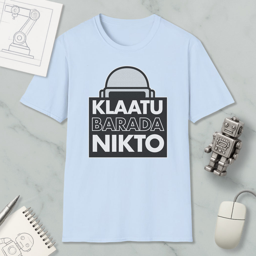 A light blue t-shirt with a graphic design featuring the text "KLATU BARADA NIKTO" in bold black letters. The t-shirt is displayed on a marble surface, along with a small robot toy and a computer mouse.