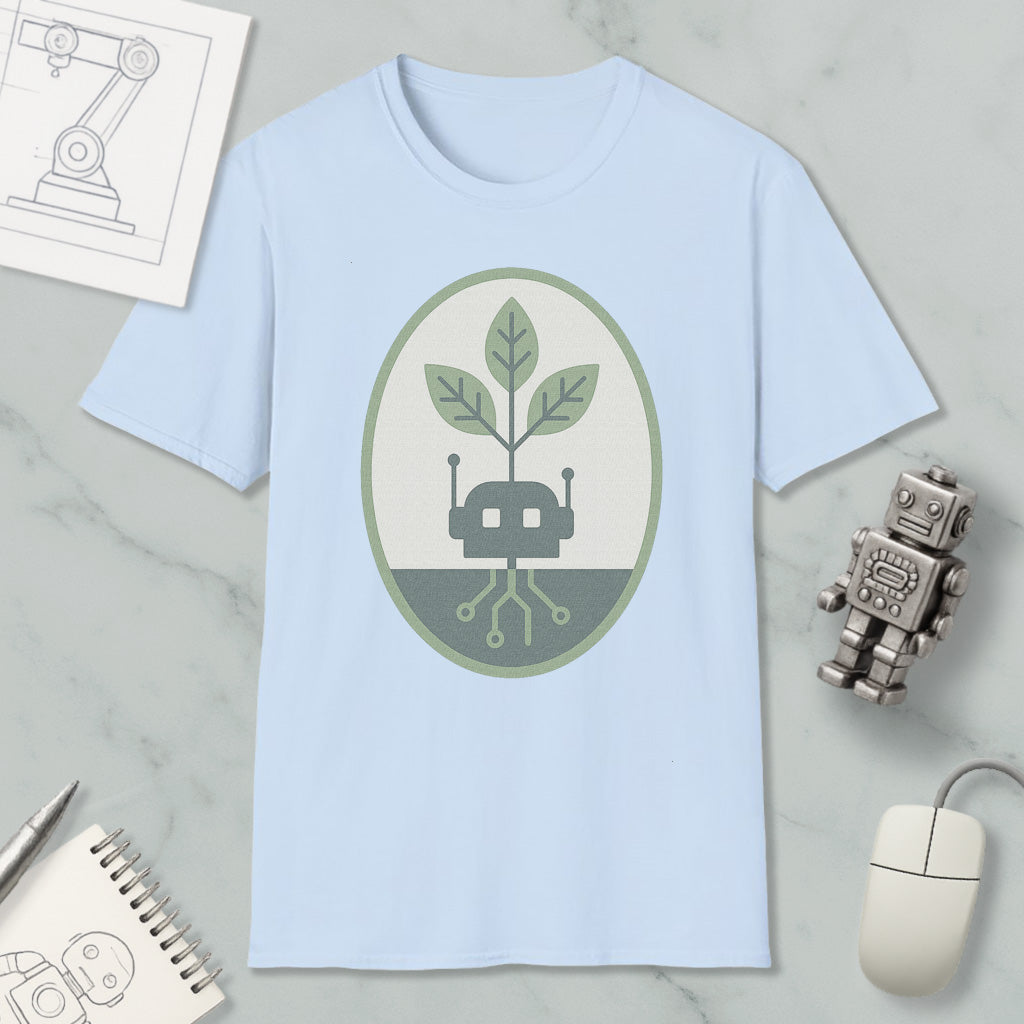 a light blue t-shirt with a graphic design of a plant growing out of a circuit board, surrounded by a green and gray oval. The t-shirt is placed on a marble surface, along with a small robot toy, a computer mouse, and a notebook.