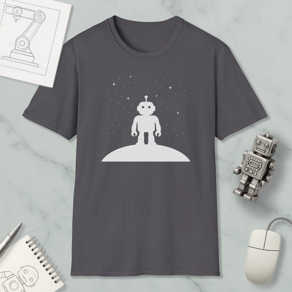 a gray t-shirt with a white robot standing on a planet, surrounded by a starry night sky. The t-shirt is placed on a marble surface, with a computer mouse, a notebook, and a robot figurine nearby.