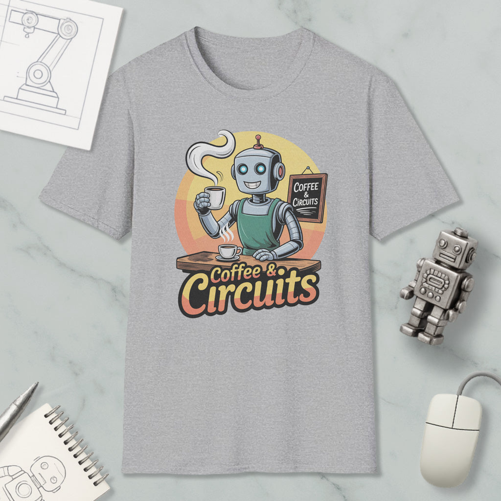 a gray t-shirt with a graphic design depicting a robot holding a cup of coffee and a sign that says "Coffee & Circuits". The t-shirt is surrounded by various objects, including a computer mouse, a notebook, and a robot figurine.