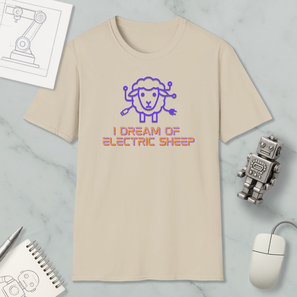 a beige t-shirt with a cartoon sheep design and the text "I DREAM OF ELECTRIC SHEEP?" printed on it. The t-shirt is placed on a marble surface, along with a computer mouse, a pen, and a notebook.