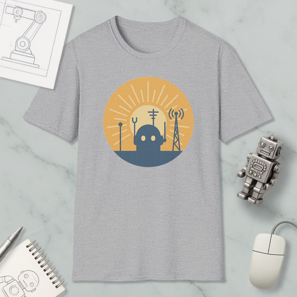 a gray t-shirt with a graphic design depicting a robot and various technological elements, such as a tower and antenna, set against a sun-like background. The t-shirt is displayed on a marble surface, along with a small robot figurine, a computer mouse, and a notebook.