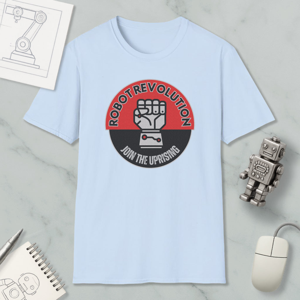 a light blue t-shirt with a graphic design that says "Robot Revolution" and "Join the Uprising", along with a fist symbol. The t-shirt is displayed on a marble surface, surrounded by various objects such as a computer mouse, a pen, a notebook, and a robot figurine.