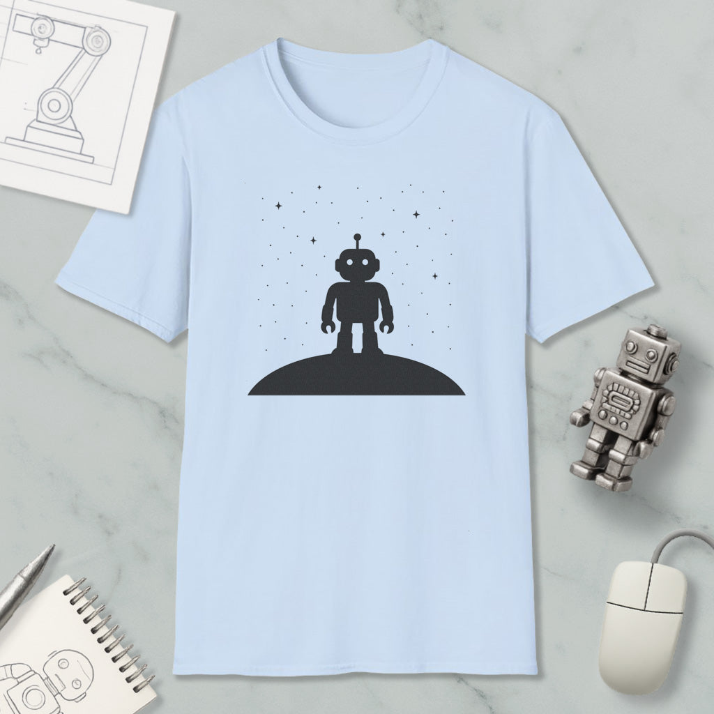 a light blue t-shirt with a black silhouette of a robot standing on a hill, surrounded by stars. The t-shirt is placed on a marble surface, along with a small robot toy and a computer mouse.