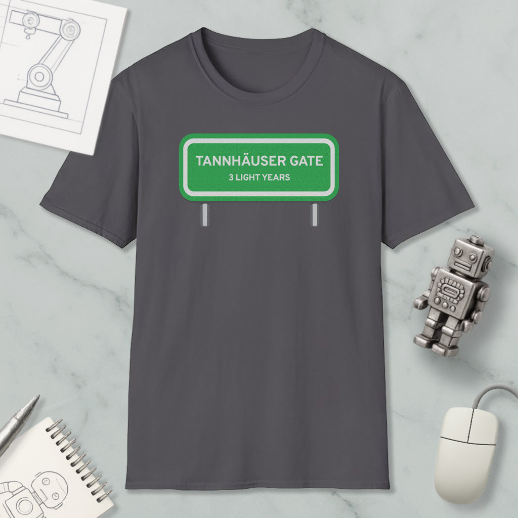 a gray t-shirt with a green road sign that reads "Tannhäuser Gate 3 Light Years" printed on it. The t-shirt is displayed on a marble surface, along with a small robot toy, a computer mouse, and a spiral notebook.