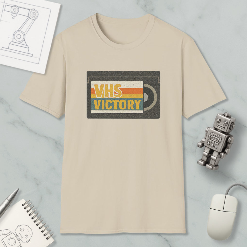 a beige t-shirt with a graphic design that says "VHS VICTORY" on it, along with a small robot and a computer mouse.