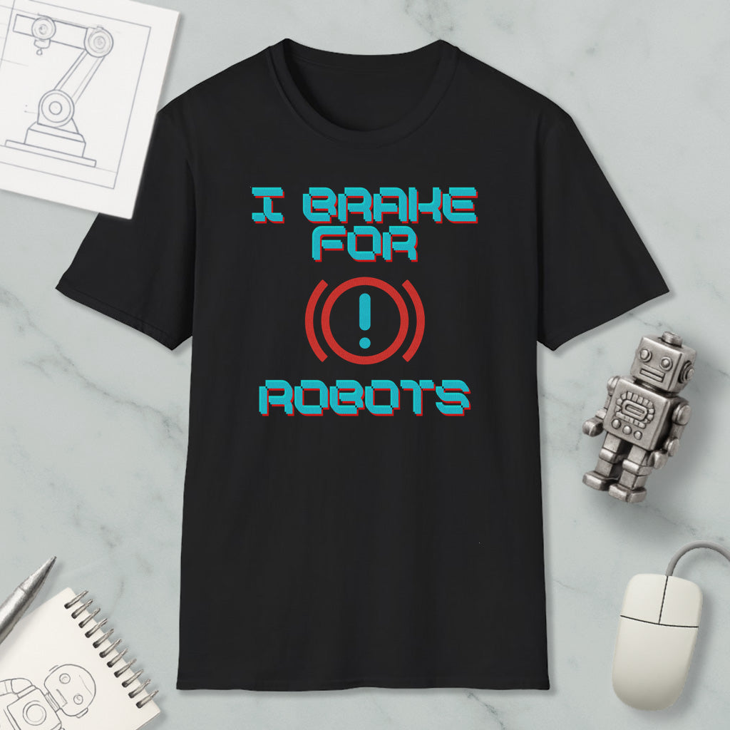 a black t-shirt with a humorous text design, a small robot, a computer mouse, and a notebook on a marble surface.