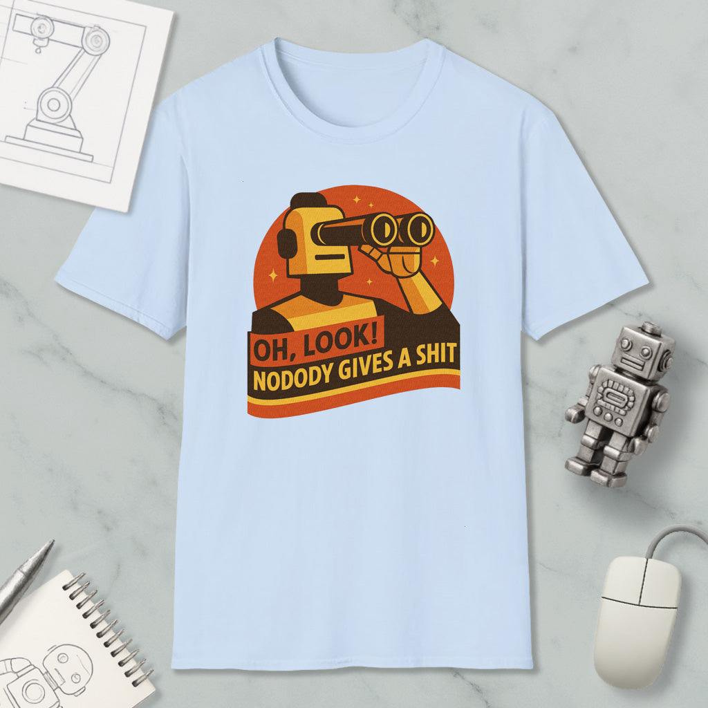 a light blue t-shirt with a graphic design depicting a robot character looking through binoculars and holding a sign that says "OH, LOOK! NODODY GIVES A SHIT". The t-shirt is displayed on a marble surface, along with a computer mouse, a pen, and a notebook.