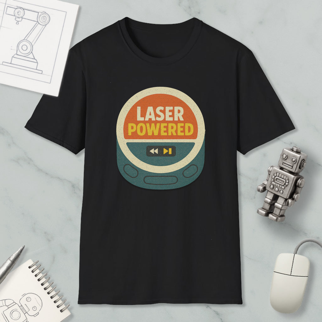 a black t-shirt with a graphic design that says "LASER POWERED" in bold letters, surrounded by a circular shape with a play button and a power symbol. The t-shirt is displayed on a marble surface, along with a small robot toy and a computer mouse.