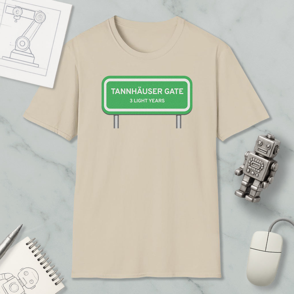 a beige t-shirt with a green road sign that reads "Tannhäuser Gate 3 Light Years" printed on it. The t-shirt is placed on a marble surface, along with a small robot toy, a computer mouse, and a notebook.