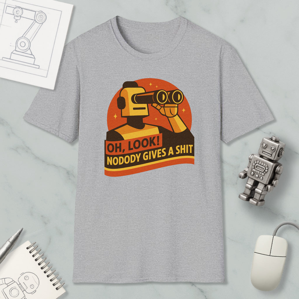 a gray t-shirt with a graphic design depicting a robot character looking through binoculars and holding a sign that says "OH, LOOK! NODODY GIVES A SHIT". The t-shirt is displayed on a marble surface, along with a computer mouse, a pen, and a notebook.
