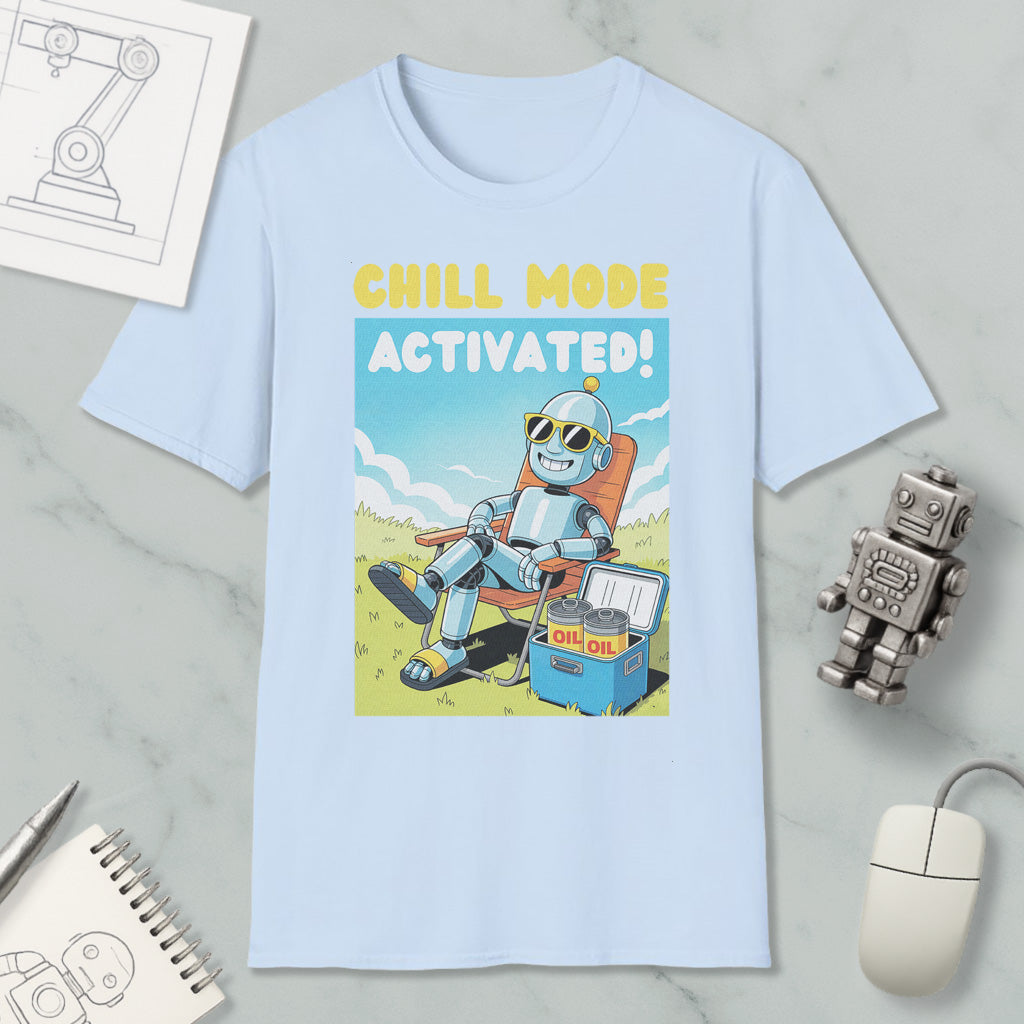 A light blue t-shirt with a cartoon robot sitting in a chair and holding a cooler, with the text "CHILL MODE ACTIVATED!" printed on it. The t-shirt is surrounded by various objects, including a computer mouse, a pen, a notebook, and a small robot figurine.