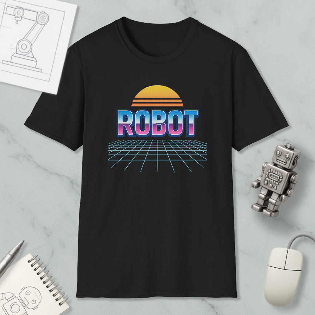 a black t-shirt with a graphic design of a robot and a sun-like shape, along with the word "ROBOT" written on it. The t-shirt is displayed on a marble surface, and there are various objects such as a computer mouse, a notebook, and a small robot figurine placed around it.