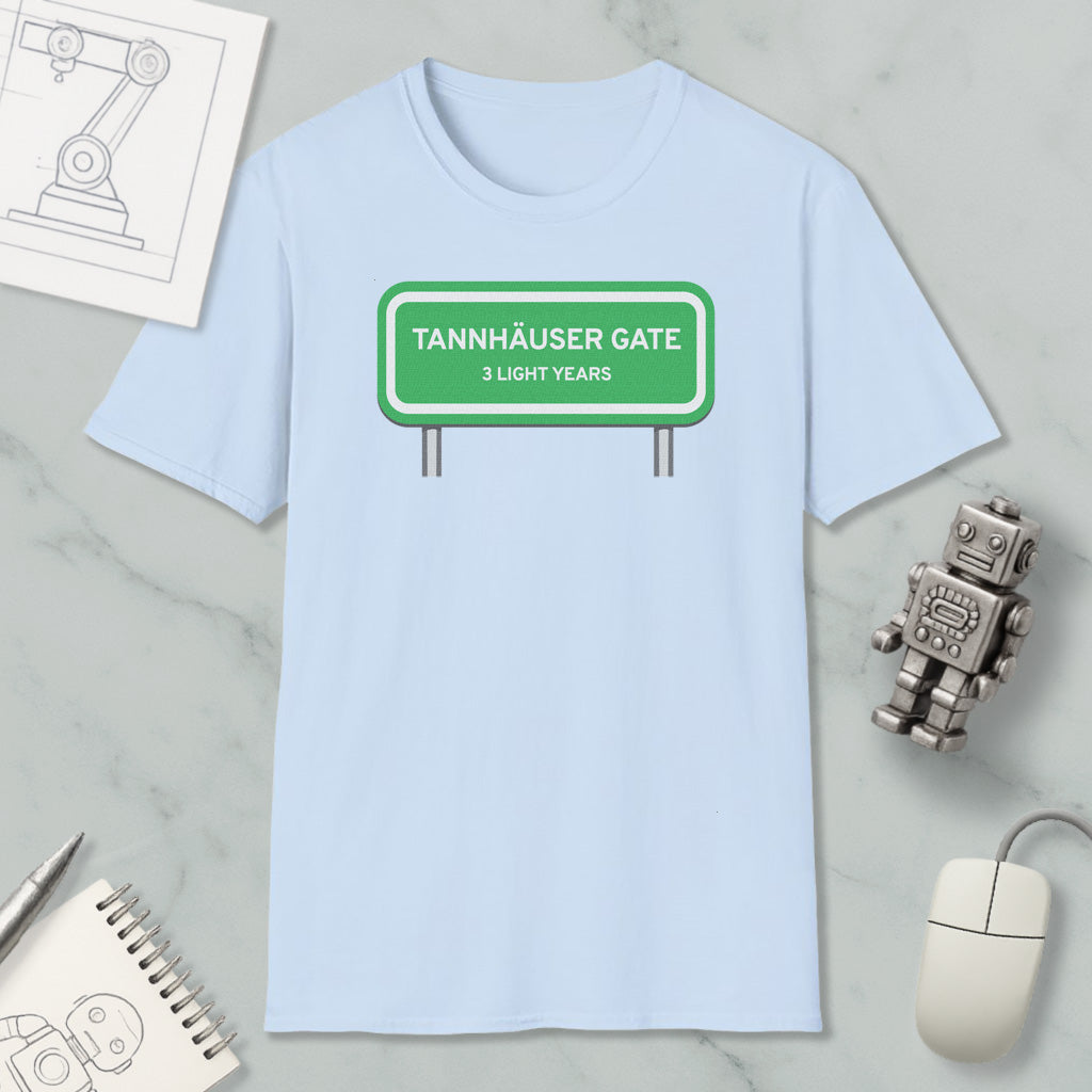 a light blue t-shirt with a green road sign that reads "Tannhäuser Gate 3 Light Years" printed on it. The t-shirt is placed on a marble surface, along with a small robot toy, a computer mouse, and a spiral notebook.