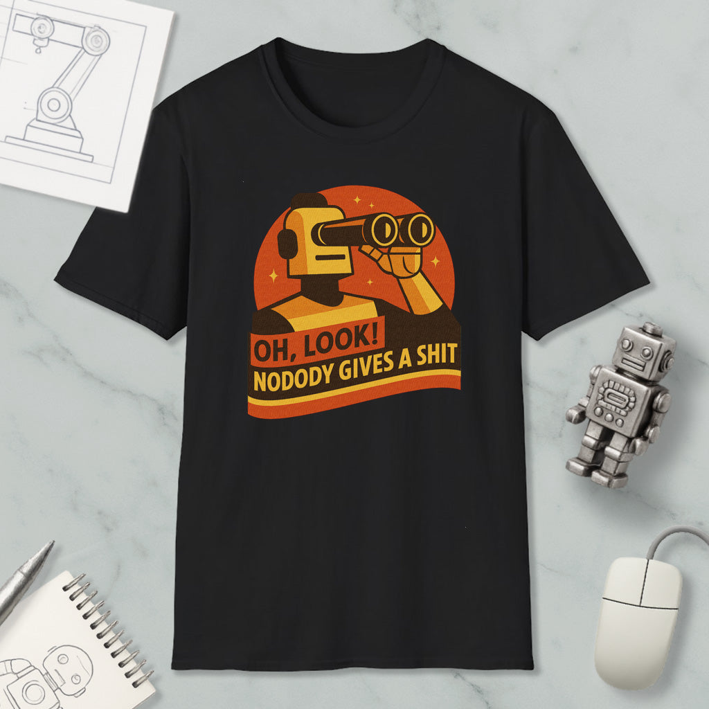 a black t-shirt with a graphic design depicting a robot character and the text "OH, LOOK! NODODY GIVES A SHIT" printed on it. The t-shirt is displayed on a marble surface, along with a computer mouse, a pen, and a notebook.