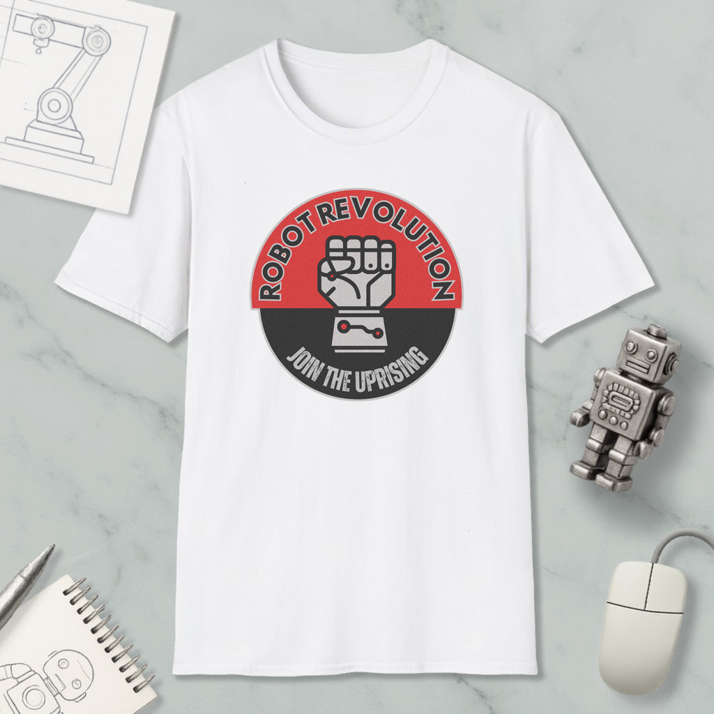 a white t-shirt with a graphic design that says "Robot Revolution" and "Join the Uprising", along with a fist symbol. The t-shirt is displayed on a marble surface, and there are various objects such as a computer mouse, a pen, and a notebook nearby.