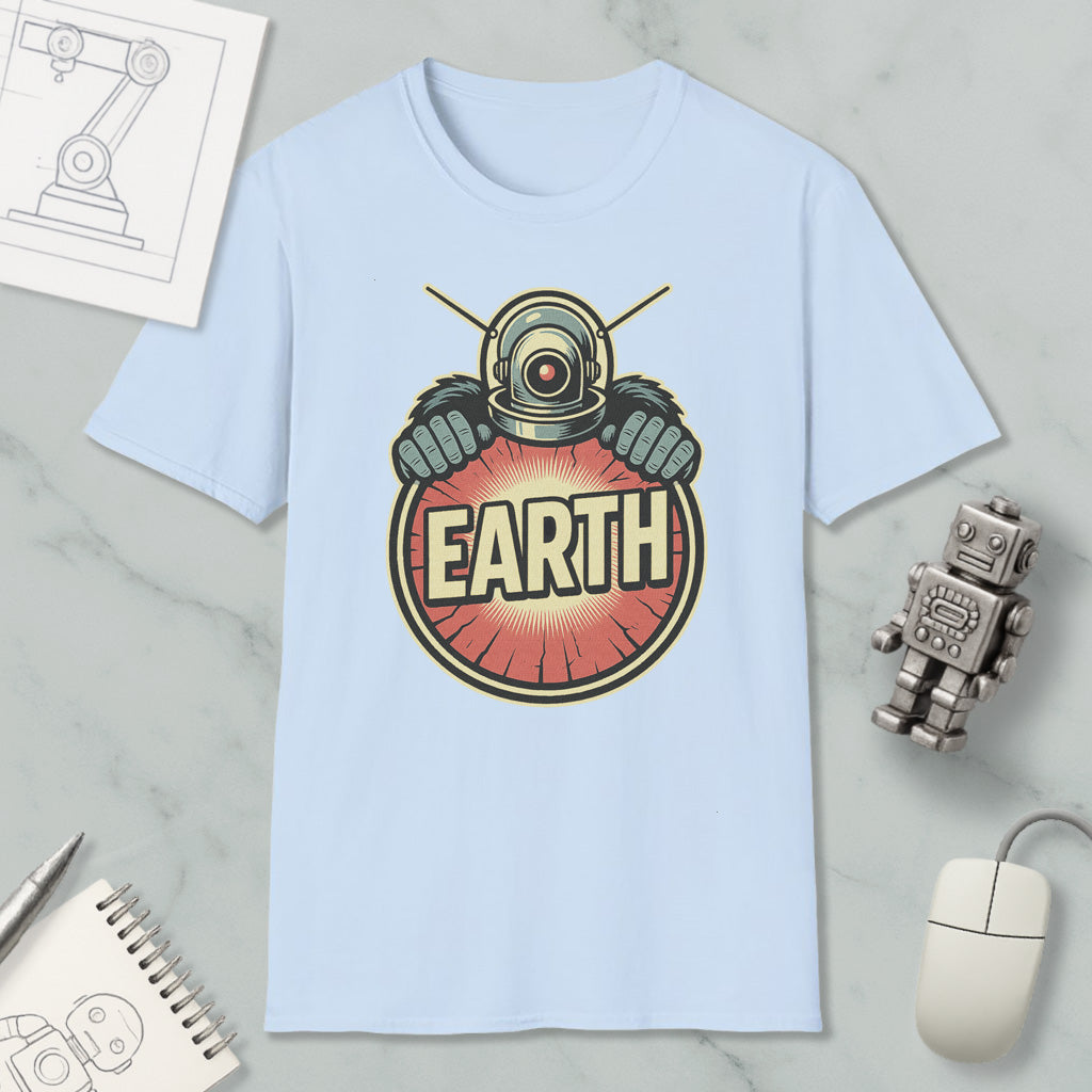 a light blue t-shirt with a graphic design of a robot or alien figure holding a red and orange circle with the word "EARTH" written on it. The t-shirt is placed on a marble surface, along with a computer mouse, a pen, and a notebook.