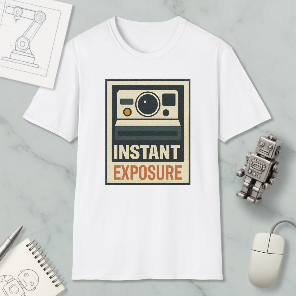 a white t-shirt with a graphic design that says "INSTANT EXPOSURE" in bold letters. The t-shirt is placed on a marble surface, surrounded by various objects such as a computer mouse, a robot, and a notebook.