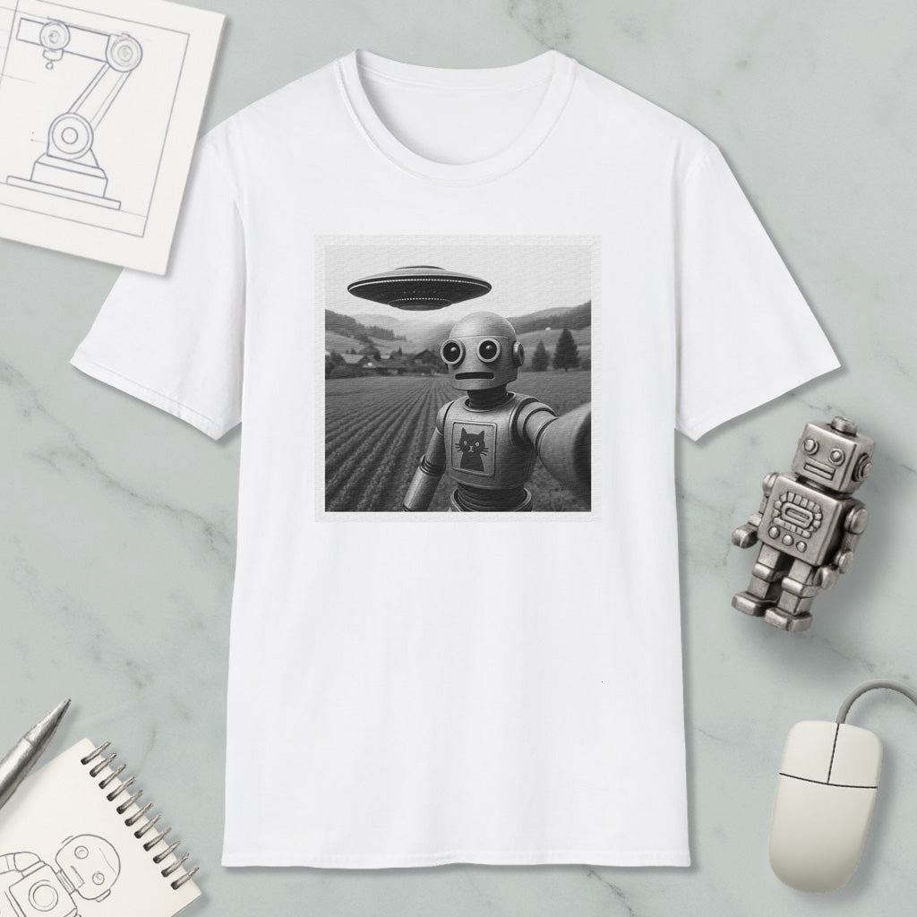 a white t-shirt with a black and white photograph of a robot standing in a field, with a large spaceship flying above it. The t-shirt is displayed on a marble surface, along with a computer mouse, a notebook, and a small robot figurine.