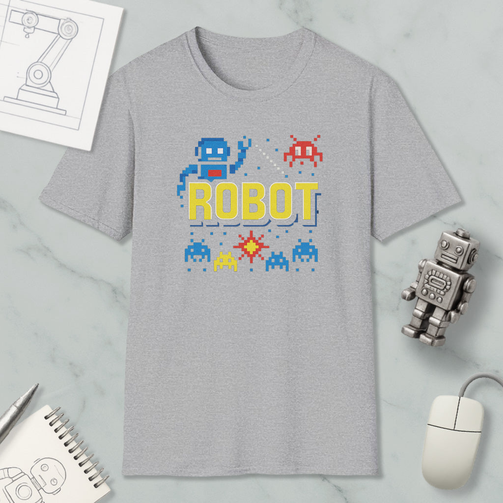 a gray t-shirt with a robot graphic and pixel art, along with a computer mouse, a notebook, and a small robot figurine.