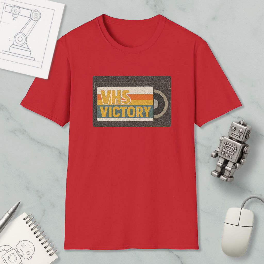 a red t-shirt with a graphic design, a computer mouse, a notebook, and a small robot on a marble surface.