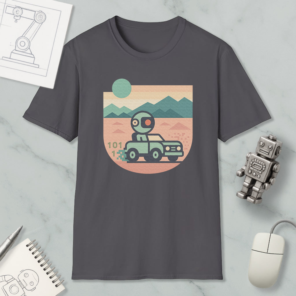 a gray t-shirt with a graphic design depicting a robot driving a car on a desert road, with mountains in the background. The t-shirt is surrounded by various objects, including a computer mouse, a notebook, and a small robot figurine.