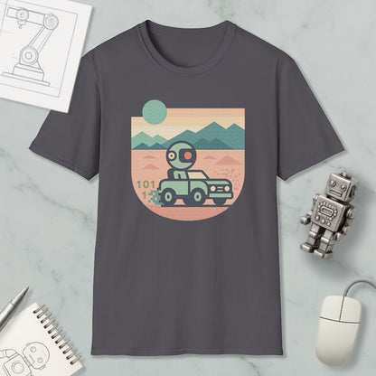 a gray t-shirt with a graphic design depicting a robot driving a car on a desert road, with mountains in the background. The t-shirt is surrounded by various objects, including a computer mouse, a notebook, and a small robot figurine.