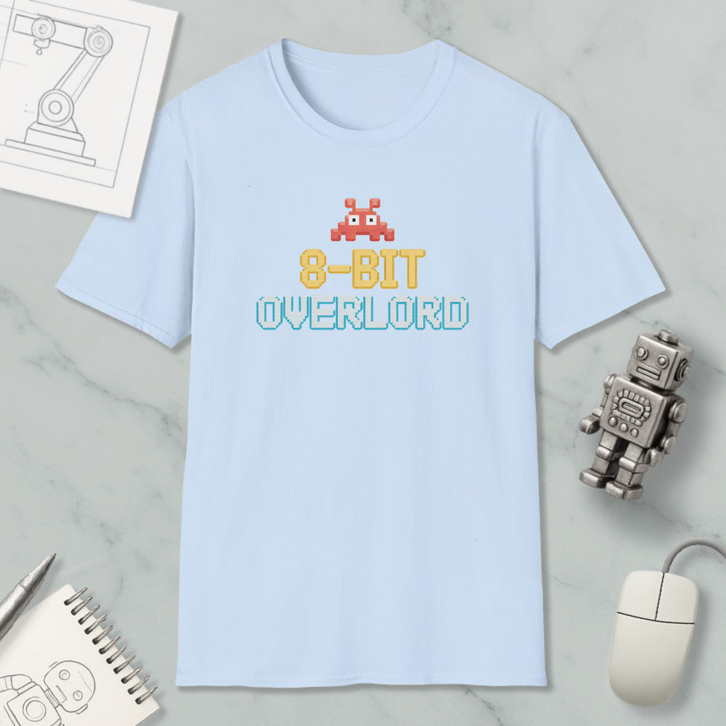 a light blue t-shirt with the text "8-BIT OVERLORD" printed on it, along with a small robot figure. The t-shirt is placed on a marble surface, and there are various objects such as a computer mouse, a spiral notebook, and a sketch of a robot figure nearby.
