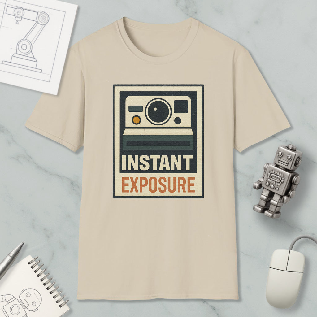 a beige t-shirt with a graphic design of a camera and the text "INSTANT EXPOSURE" printed on it, along with a small robot and a computer mouse.
