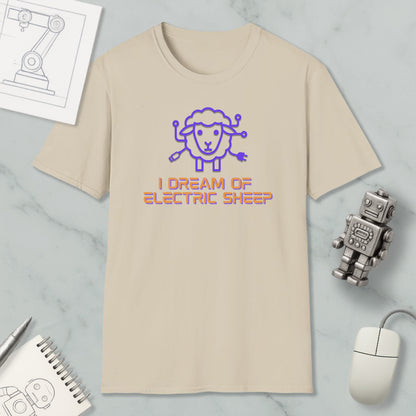 a beige t-shirt with a cartoon sheep design and the text "I DREAM OF ELECTRIC SHEEP?" printed on it. The t-shirt is placed on a marble surface, along with a computer mouse, a pen, and a notebook.