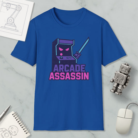 a blue t-shirt with a graphic design of a character resembling a video game arcade game character, along with the text "ARCADE ASSASSIN" printed on it. The t-shirt is displayed on a marble surface, and there are various objects such as a computer mouse, a pen, and a notebook in the background.