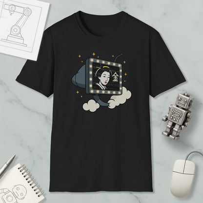 a black t-shirt with a graphic design depicting a woman's face inside a television set, surrounded by clouds and stars. The t-shirt is placed on a marble surface, with a computer mouse, a notebook, and a robot figurine nearby.