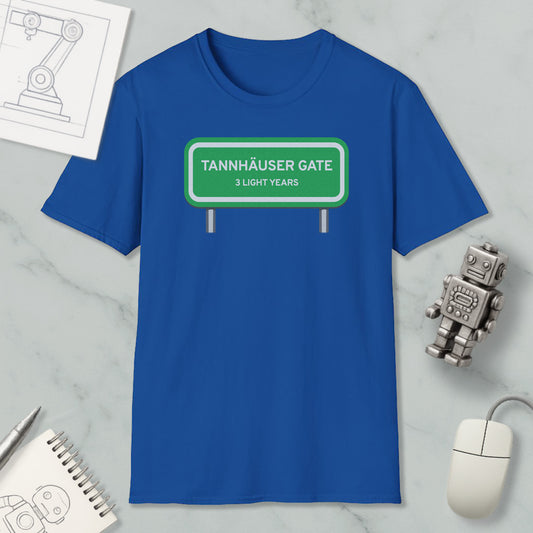 a blue t-shirt with a green road sign that reads "Tannhäuser Gate" and "3 light years" printed on it. The t-shirt is placed on a marble surface, along with a computer mouse, a spiral notebook, and a small robot figurine.