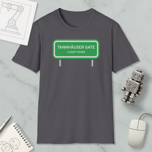 a gray t-shirt with a green road sign that reads "Tannhäuser Gate 3 Light Years" printed on it. The t-shirt is displayed on a marble surface, along with a small robot toy, a computer mouse, and a spiral notebook.