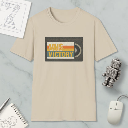 a beige t-shirt with a graphic design that says "VHS VICTORY" on it, along with a small robot and a computer mouse.