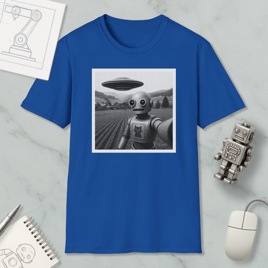 a blue t-shirt with a black and white photograph of a robot standing in a field, with a large spaceship flying above it. The t-shirt is displayed on a marble surface, along with a computer mouse, a notebook, and a small robot figurine.