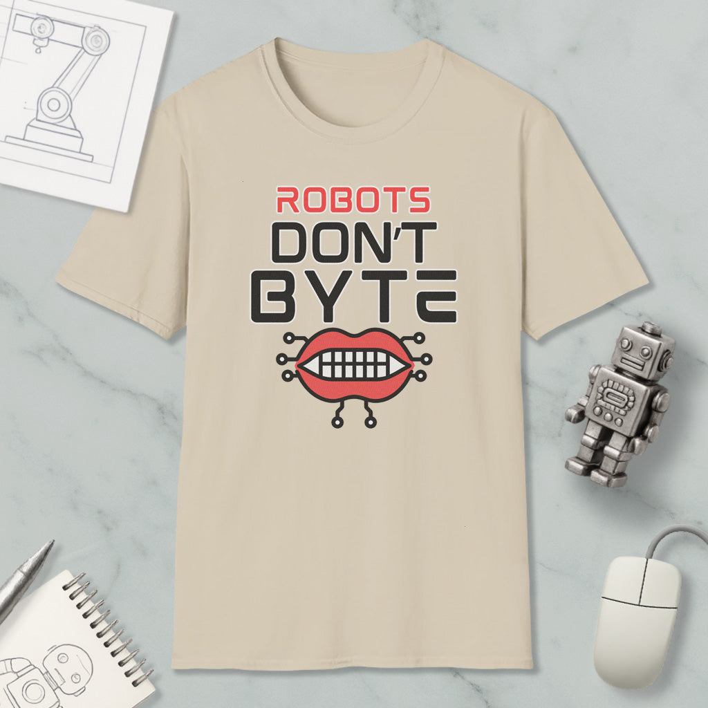 a beige t-shirt with a graphic design that says "ROBOTS DON'T BYTE" and includes a robot mouth with teeth. The t-shirt is placed on a marble surface, along with a computer mouse, a notebook, and a small robot figurine.