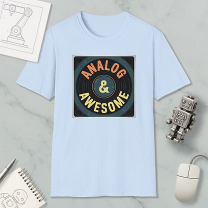 a light blue t-shirt with a graphic design that says "ANALOG & AWESOME" in bold letters. The t-shirt is placed on a marble surface, surrounded by various objects such as a computer mouse, a robot, and a notebook.
