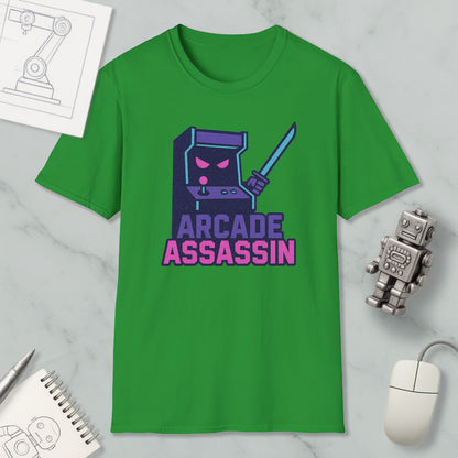 a green t-shirt with a graphic design of a character resembling a video game arcade machine, along with the text "ARCADE ASSASSIN" printed on it. The t-shirt is displayed on a marble surface, and there are various objects such as a computer mouse, a pen, and a notebook nearby.