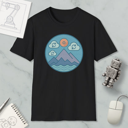 a black t-shirt with a circular graphic design depicting mountains, clouds, and a sun. Surrounding the t-shirt are various objects, including a computer mouse, a notebook, and a robot figurine.