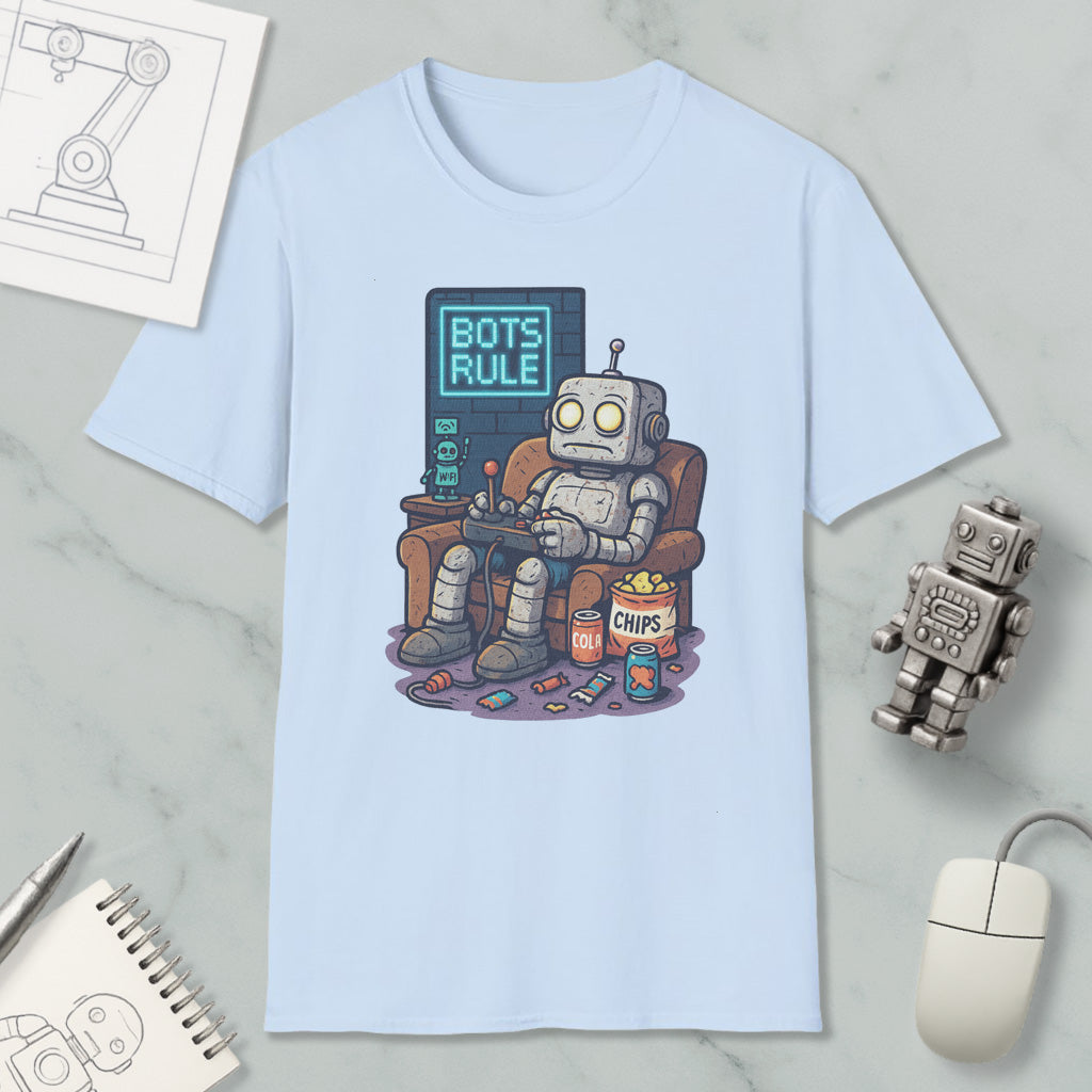 A light blue t-shirt with a cartoon robot sitting in a chair and playing a video game, with a sign that says "BOTS RULE". The t-shirt is surrounded by various objects, including a computer mouse, a notebook, and a small robot figurine.