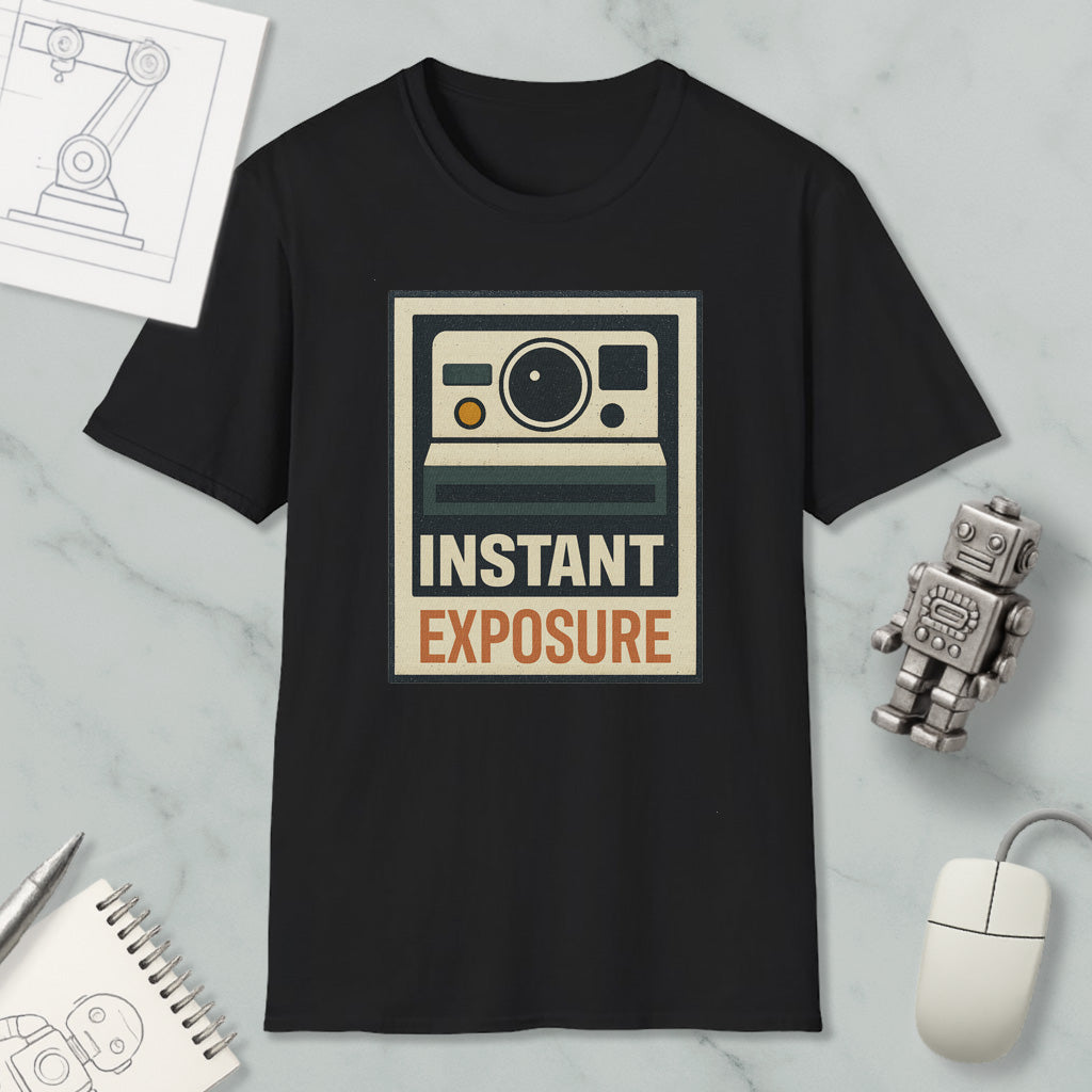 a black t-shirt with a graphic design that says "INSTANT EXPOSURE" in bold letters. The t-shirt is displayed on a marble surface, along with a small robot toy and a computer mouse.