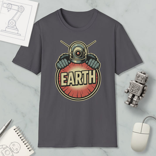 a gray t-shirt with a graphic design of a robot or alien figure holding a red circle with the word "EARTH" written on it. The t-shirt is displayed on a marble surface, along with a computer mouse, a notebook, and a small robot figurine.