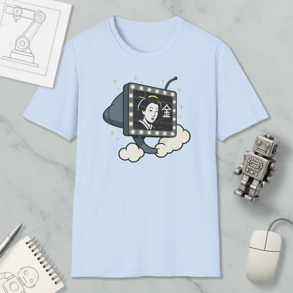 a light blue t-shirt with a graphic design depicting a woman's face on a television screen, surrounded by clouds and stars. The t-shirt is placed on a marble surface, with a computer mouse, a robot, and a notebook nearby.