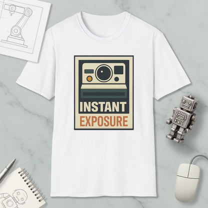 a white t-shirt with a graphic design that says "INSTANT EXPOSURE" in bold letters. The t-shirt is placed on a marble surface, surrounded by various objects such as a computer mouse, a robot, and a notebook.